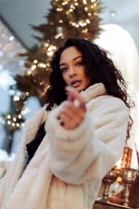 woman in a fuzzy white coat smiling with lights in the background