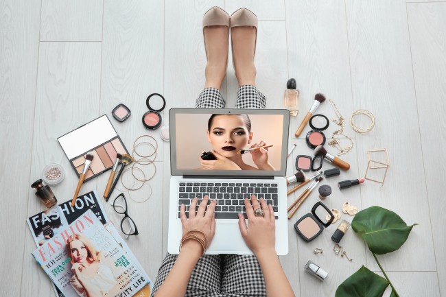 woman surrounded by makeup with laptop on her legs